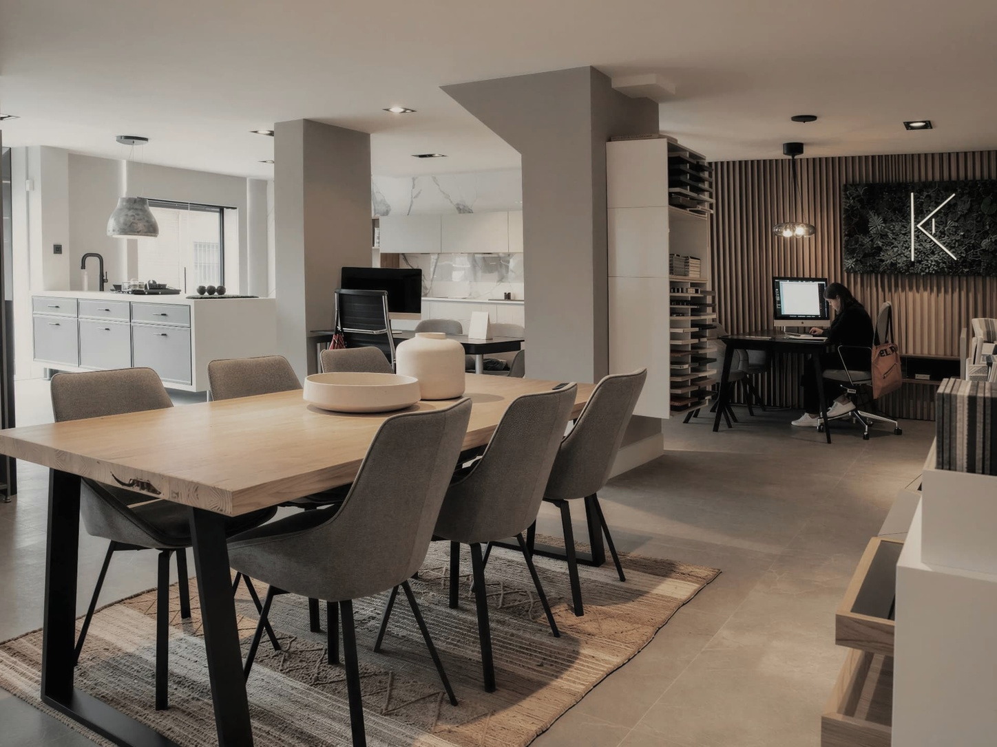 Sala del estudio de Madrid con gran mesa de roble, cocinas expuestas al fondo y la biblioteca de muestras junto al puesto de trabajo