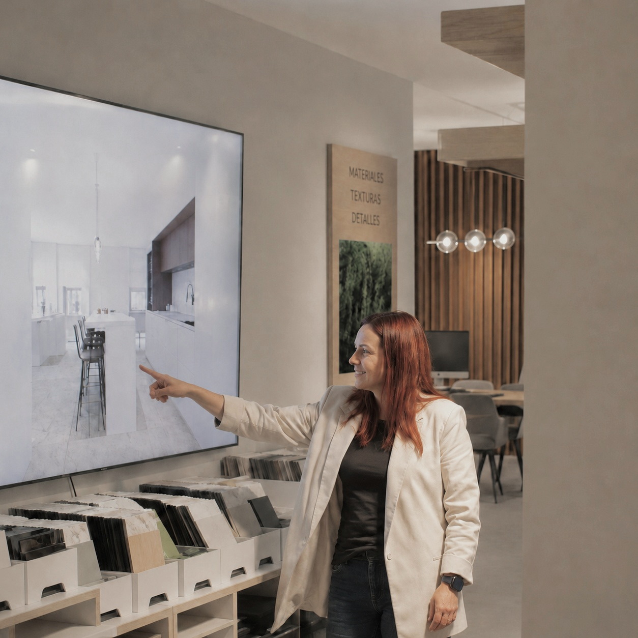 Una diseñadora del estudio señala un proyecto de cocina en la pantalla, junto a la biblioteca de muestras de materiales