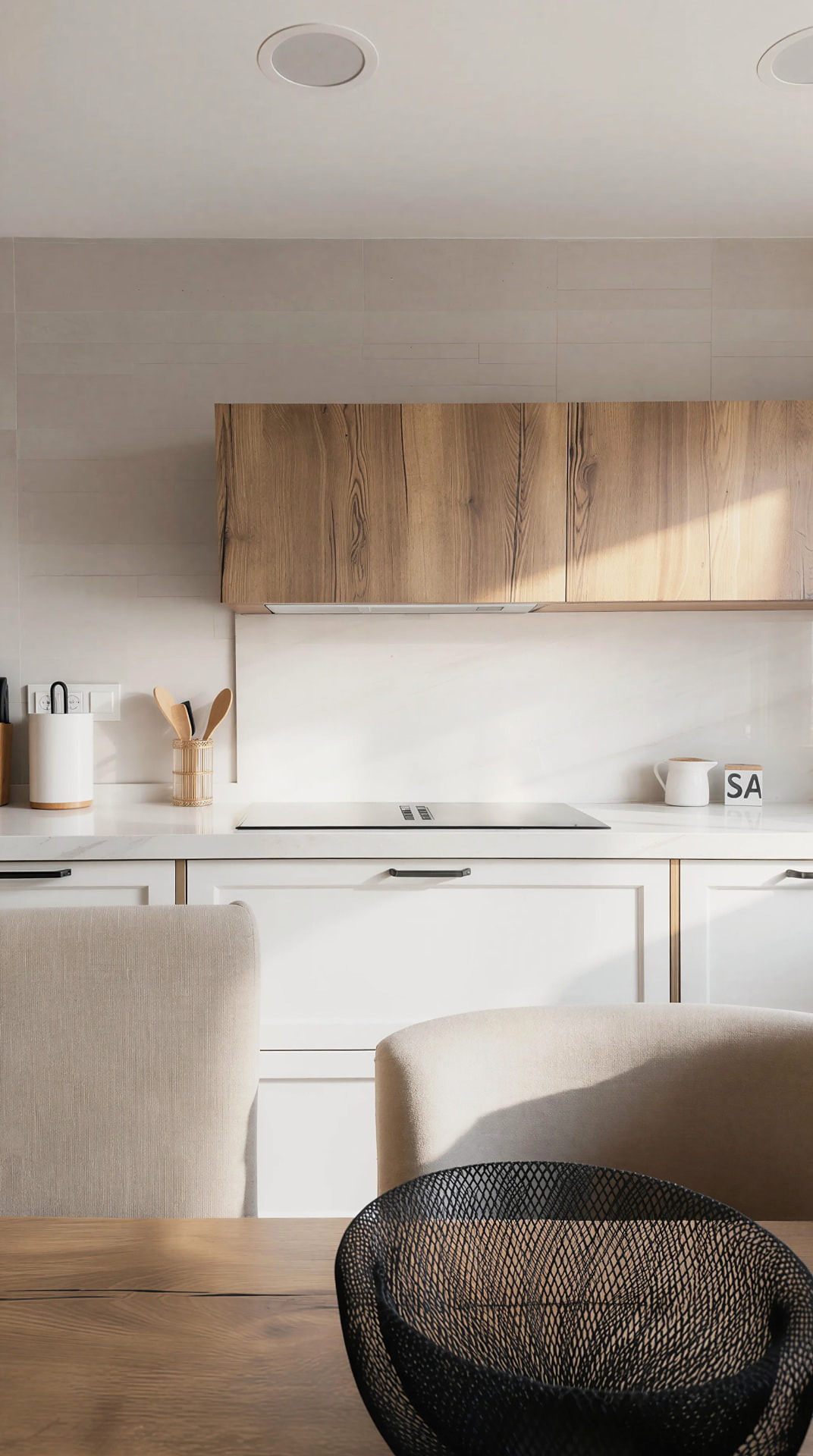 Frente blanco con módulo alto de madera y encimera clara bajo la luz de la mañana