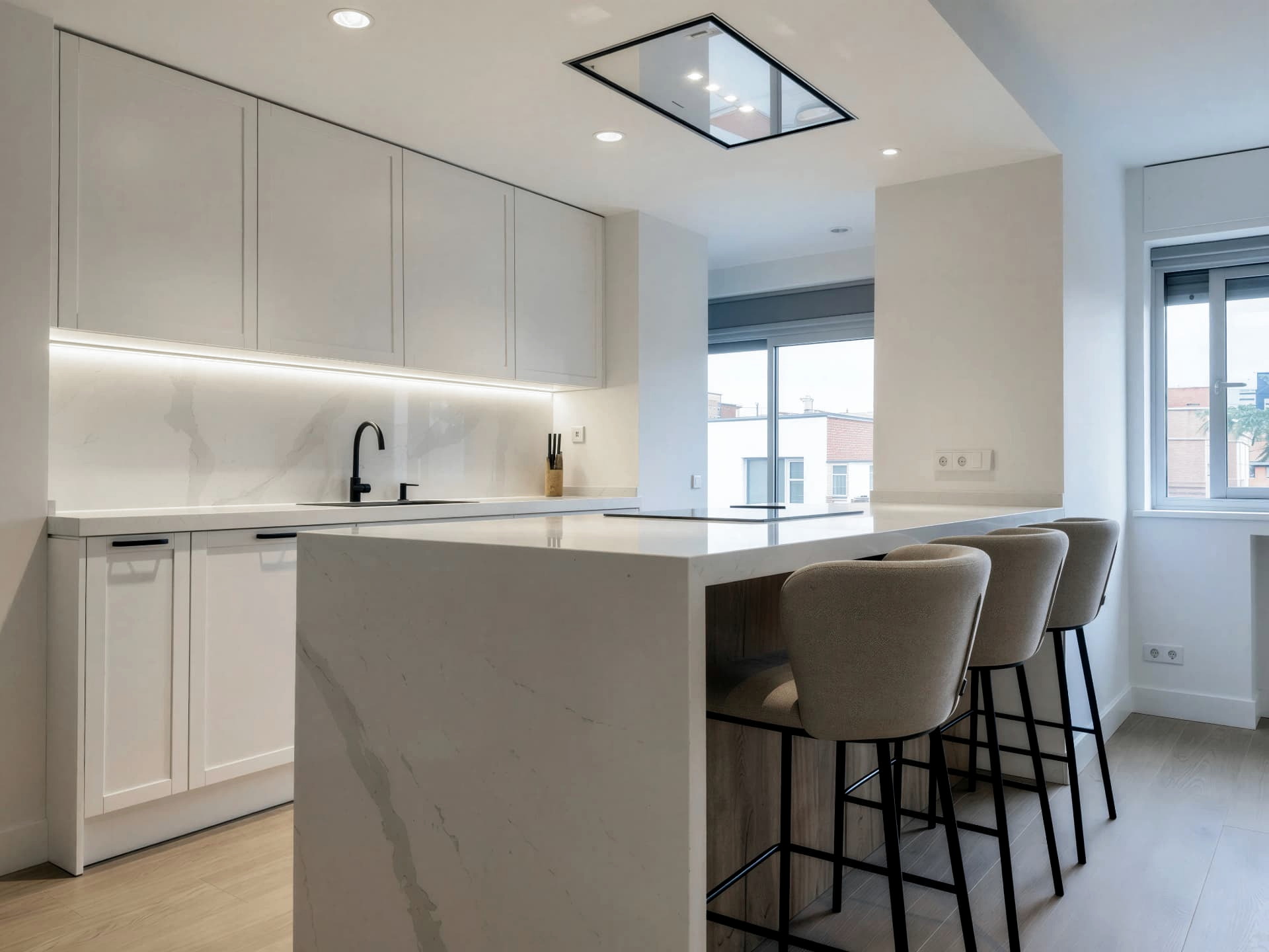 Cocina blanca con península de piedra clara veteada abierta a la ventana y al resto de la vivienda