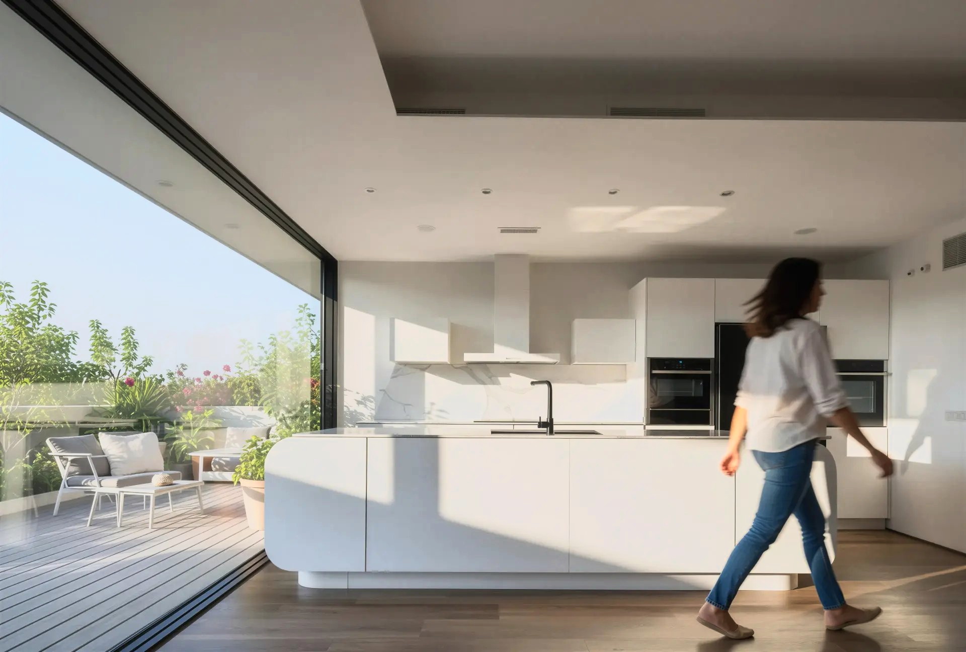 Cocina blanca con isla curva abierta a una terraza mediante un gran ventanal corredero, con una persona caminando junto a la isla