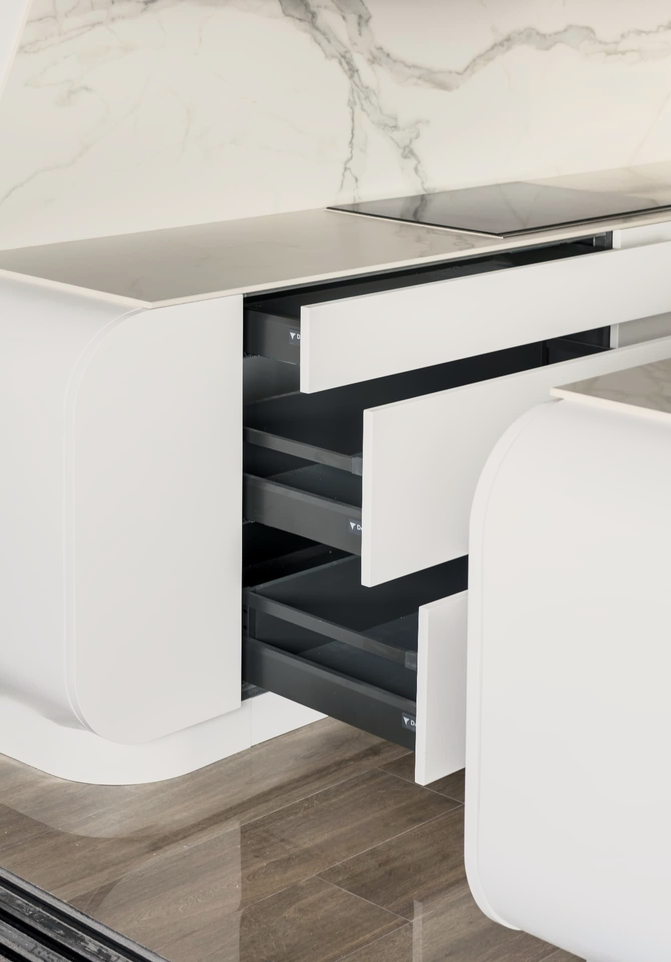 Cajones interiores abiertos bajo la encimera, entre los costados curvos del mueble blanco