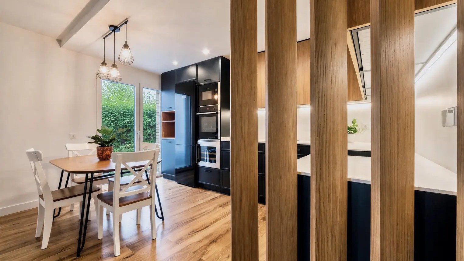 Vista de la cocina a través de la celosía de roble, con el comedor a la izquierda y la columna de aparatos al fondo
